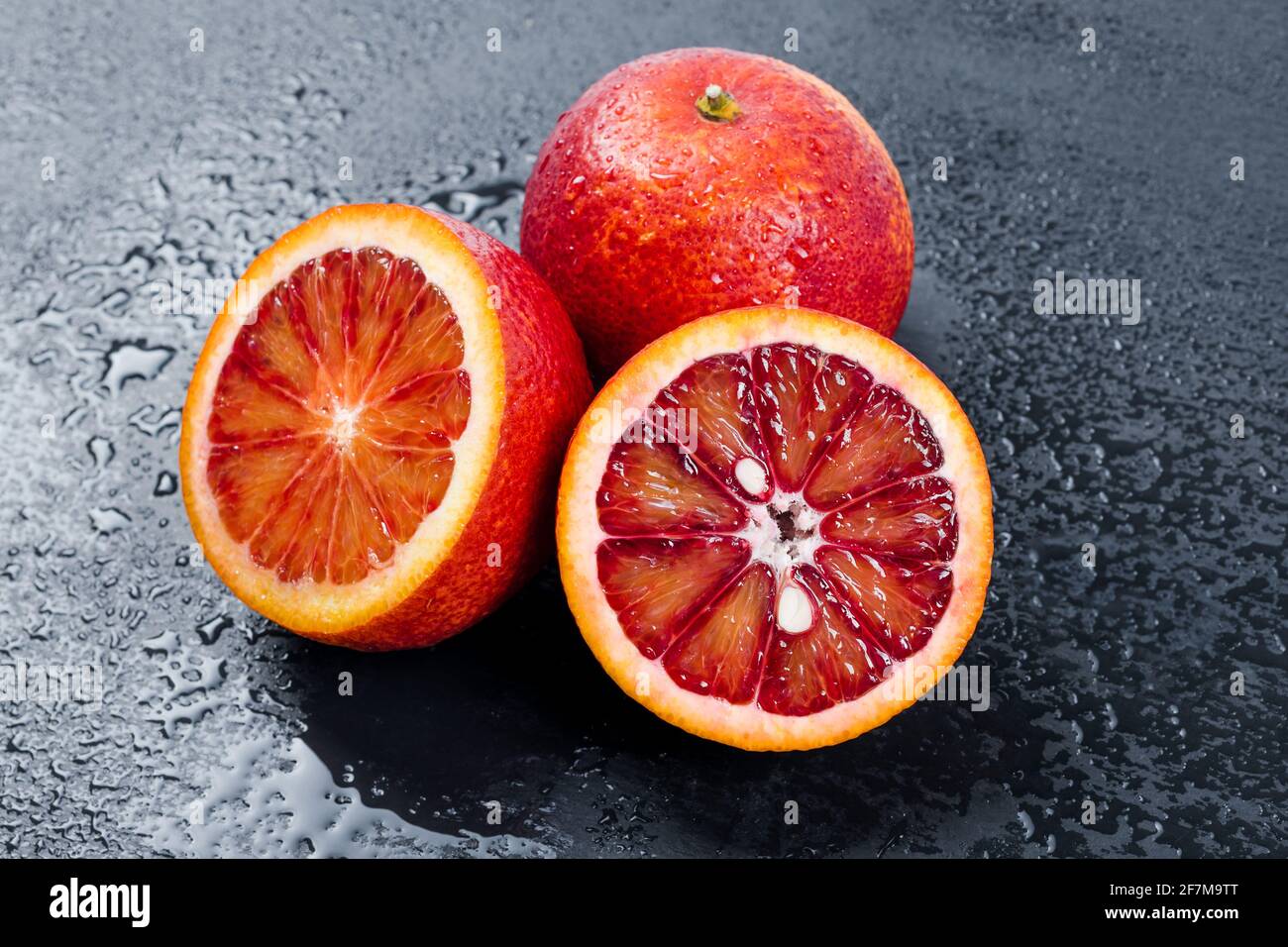 Blutige Orangen ganz und halbiert auf schwarzem Schieferbrett mit Wassertropfen. Rote sizilianische Orangenfrucht. Stockfoto