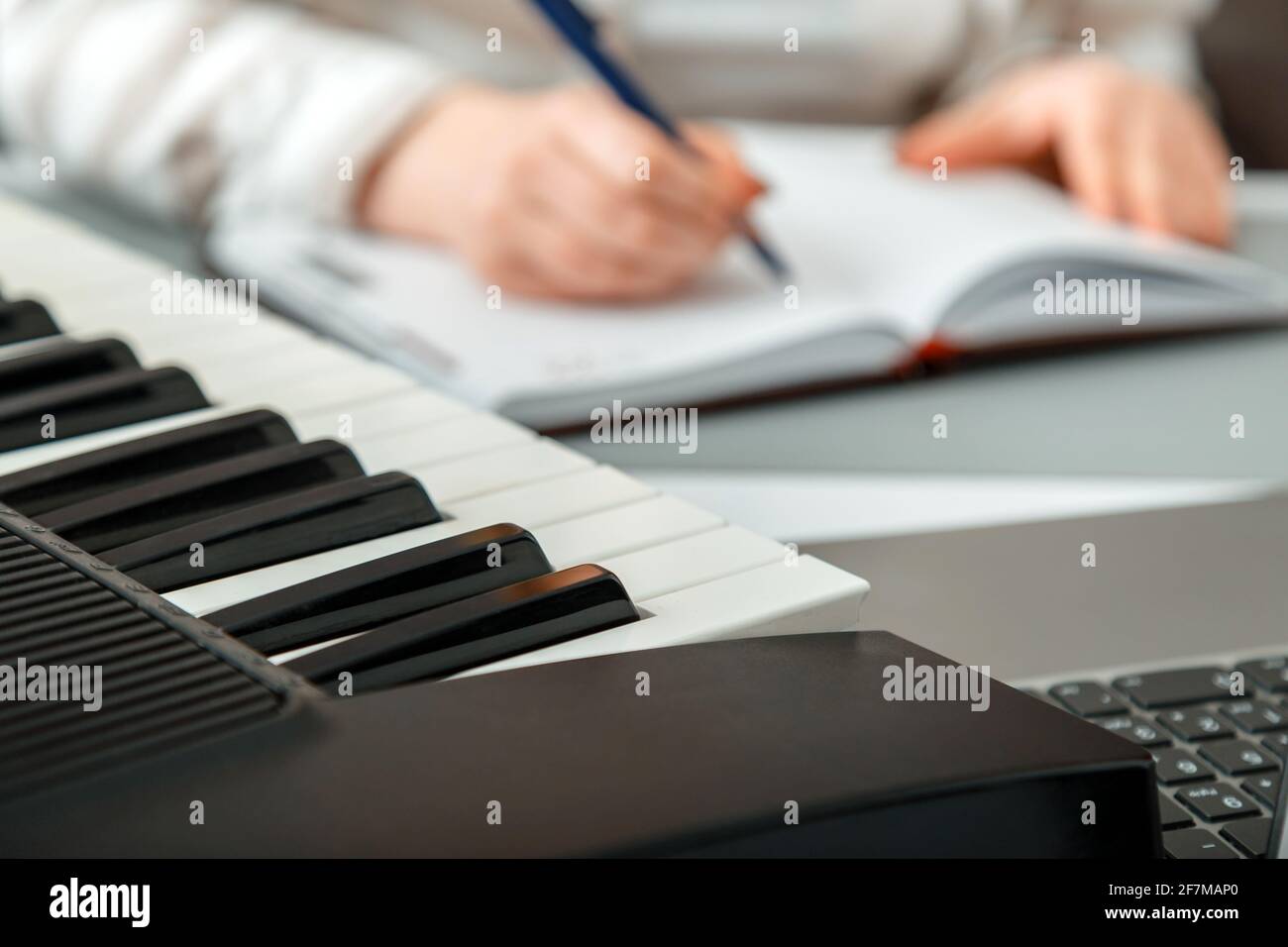 Frau komponiert Musik, weibliche Hände schreiben Notizen oder Lieder in ein Musikbuch. Teen Mädchen lernt, Klaviermusik zu spielen, macht Notizen im Notizbuch. Synthesizer-Klavier Stockfoto