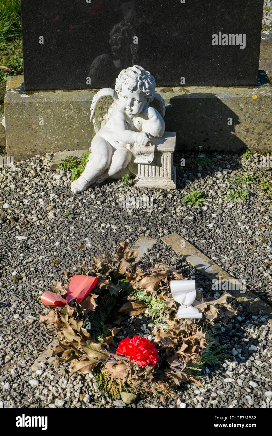 Eine Statue eines verzweifelten geflügelten Cherubs überblickt einen verdorrten Weihnachtskränz auf einem Grab auf einem irischen Friedhof Stockfoto
