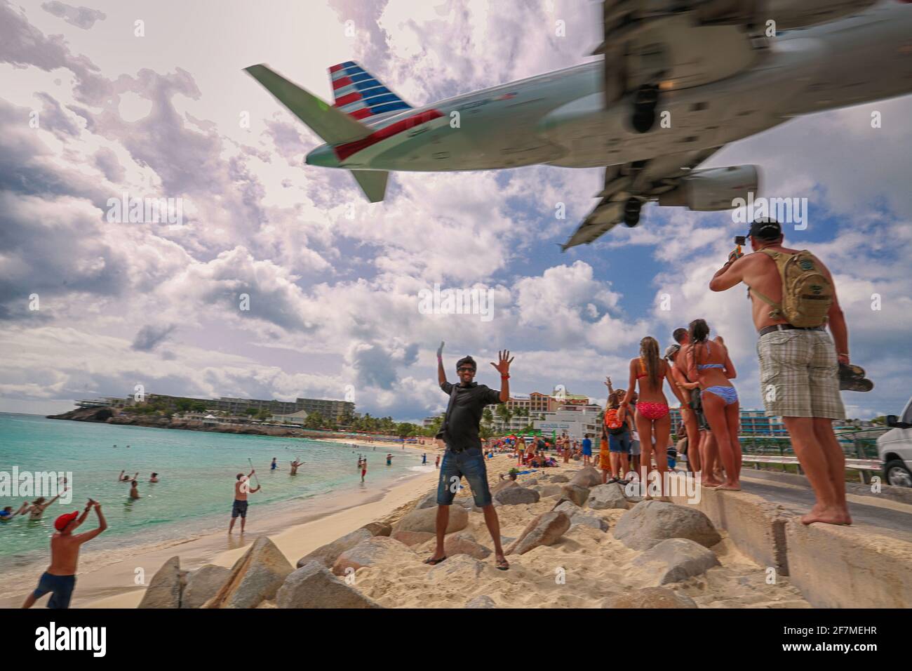 Hinter einem jungen Mann hebt das Flugzeug auf dem Hintergrund ab. Ein junger Mann steht und posiert am Strand in der Nähe des Flughafens und spreizte die Arme zum Fliegen. Stockfoto