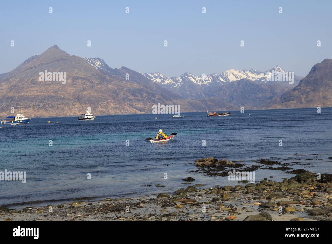 Eineineinee Kajaker mit Blick auf das Meer mit Cuillin Hills mit Schnee im Hintergrund, Strand im Vordergrund Stockfoto