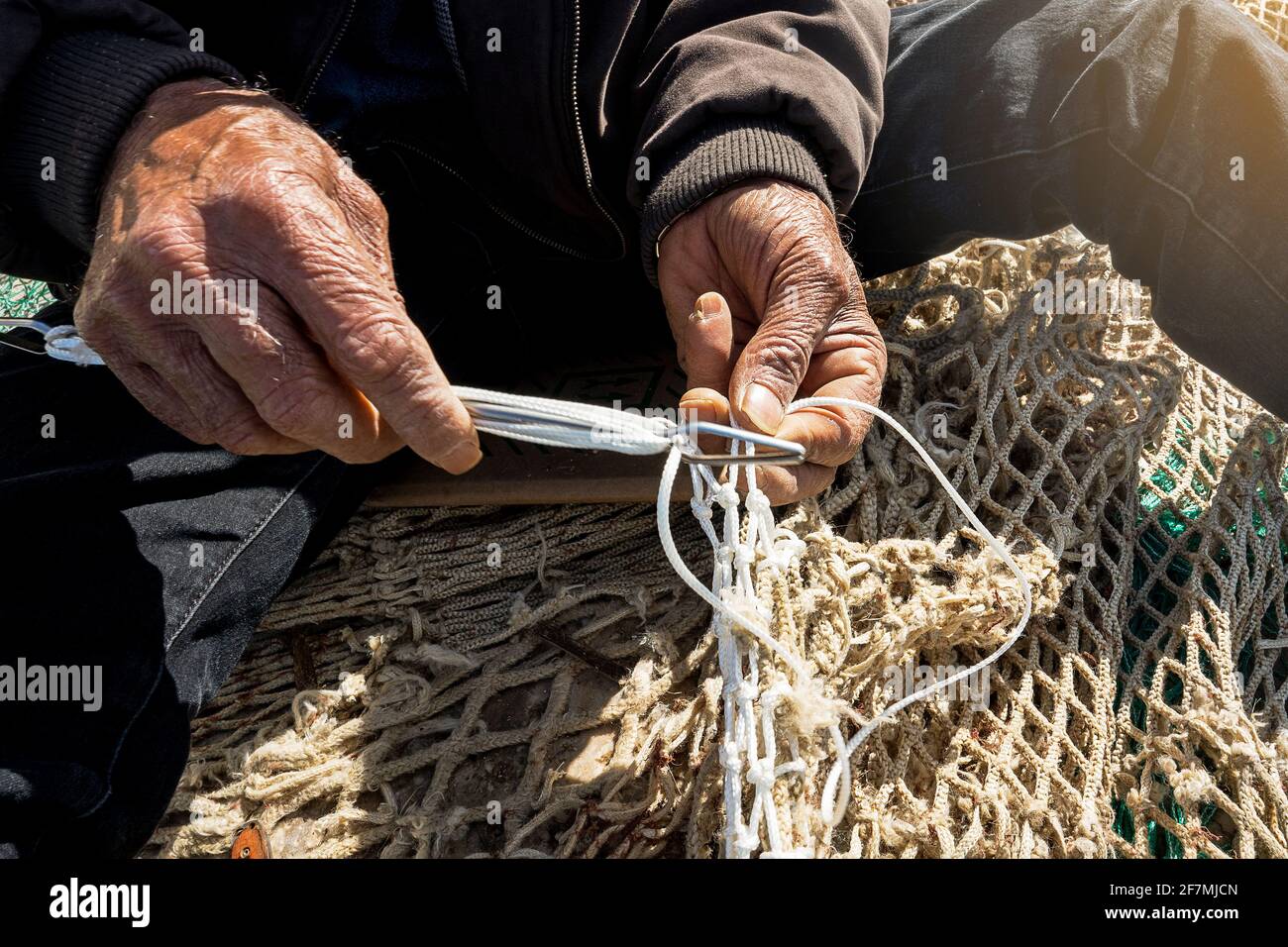 Alte Fischer Hand näht ein Fischernetz auf dem Pier. Verloren traditionelle Arbeit Stockfoto