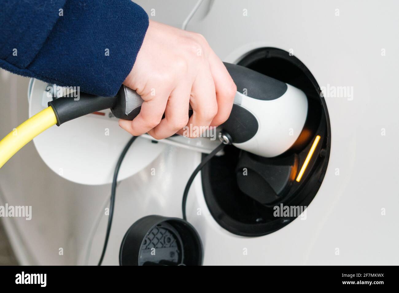 Frau führt das Netzkabel in ein Elektroauto ein Zum Aufladen Stockfoto