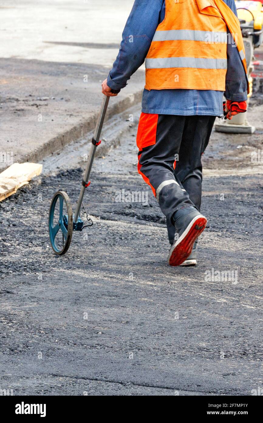 Ein Straßendienstmitarbeiter misst die Baustelle mit einem elektronischen Messrad. Stockfoto