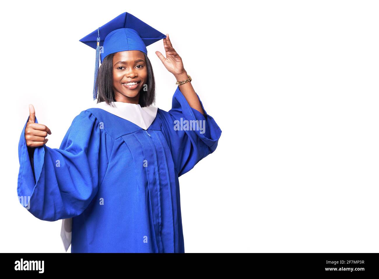 Afroamerikanische schöne Frau in einem blauen Gewand und Hut, auf einem weißen isolierten Hintergrund lächelt und zeigt Daumen nach oben Stockfoto