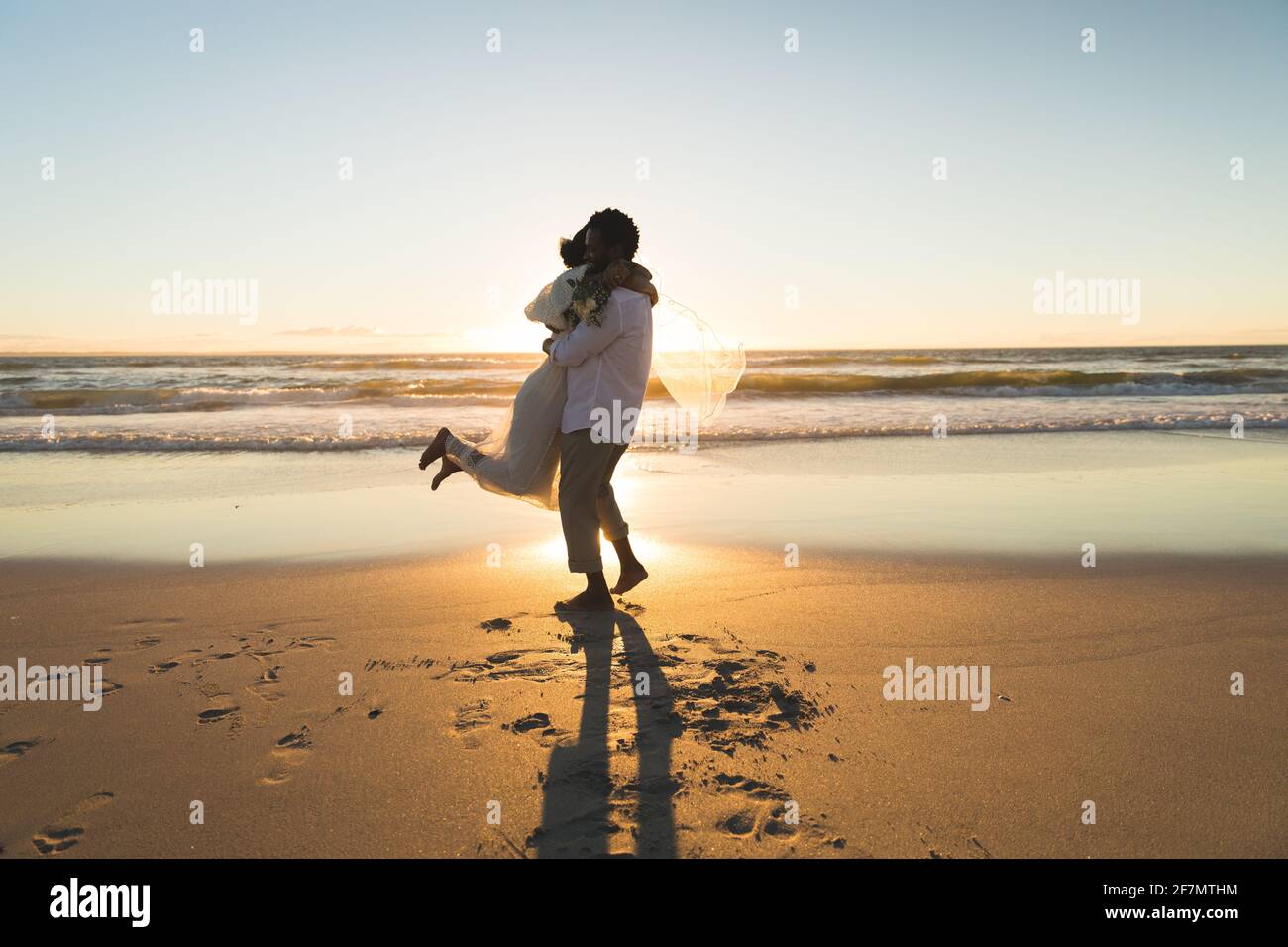 afroamerikanisches Paar verliebt sich in die Ehe und umarmt sich am Strand während des Sonnenuntergangs Stockfoto