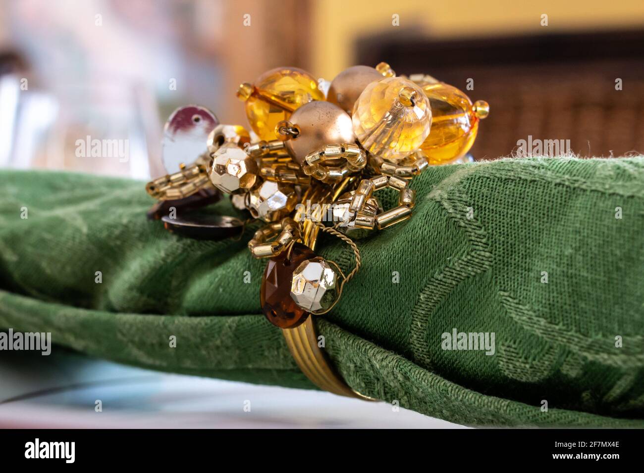 Eine aufgerollte grüne Serviette mit einem goldenen Serviettenhalter mit Bommel, horizontal auf einem fein dekorierten Tisch in Erwartung eines Geburtstagsessens. Februar 2021. Stockfoto