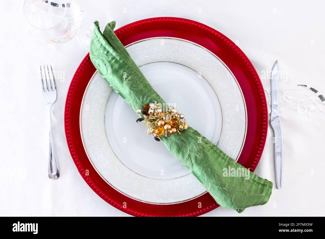 Eine grüne Serviette mit einem goldenen Serviettenring auf einer weißen Keramikplatte und weißem Tischtuch. Ort für ein Weihnachtsessen oder ein festliches Fest. Stockfoto