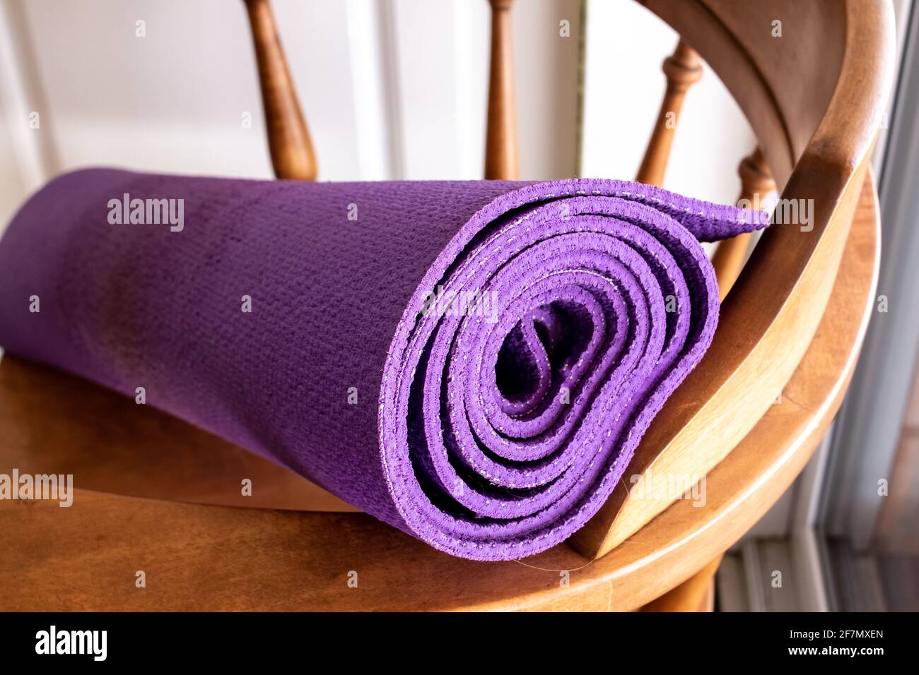 Eine purpurne Yoga-Übungsmatte, aufgerollt auf einem altmodischen Vintage-Holzstuhl in London, Ontario, Kanada, Februar 2021. Stockfoto
