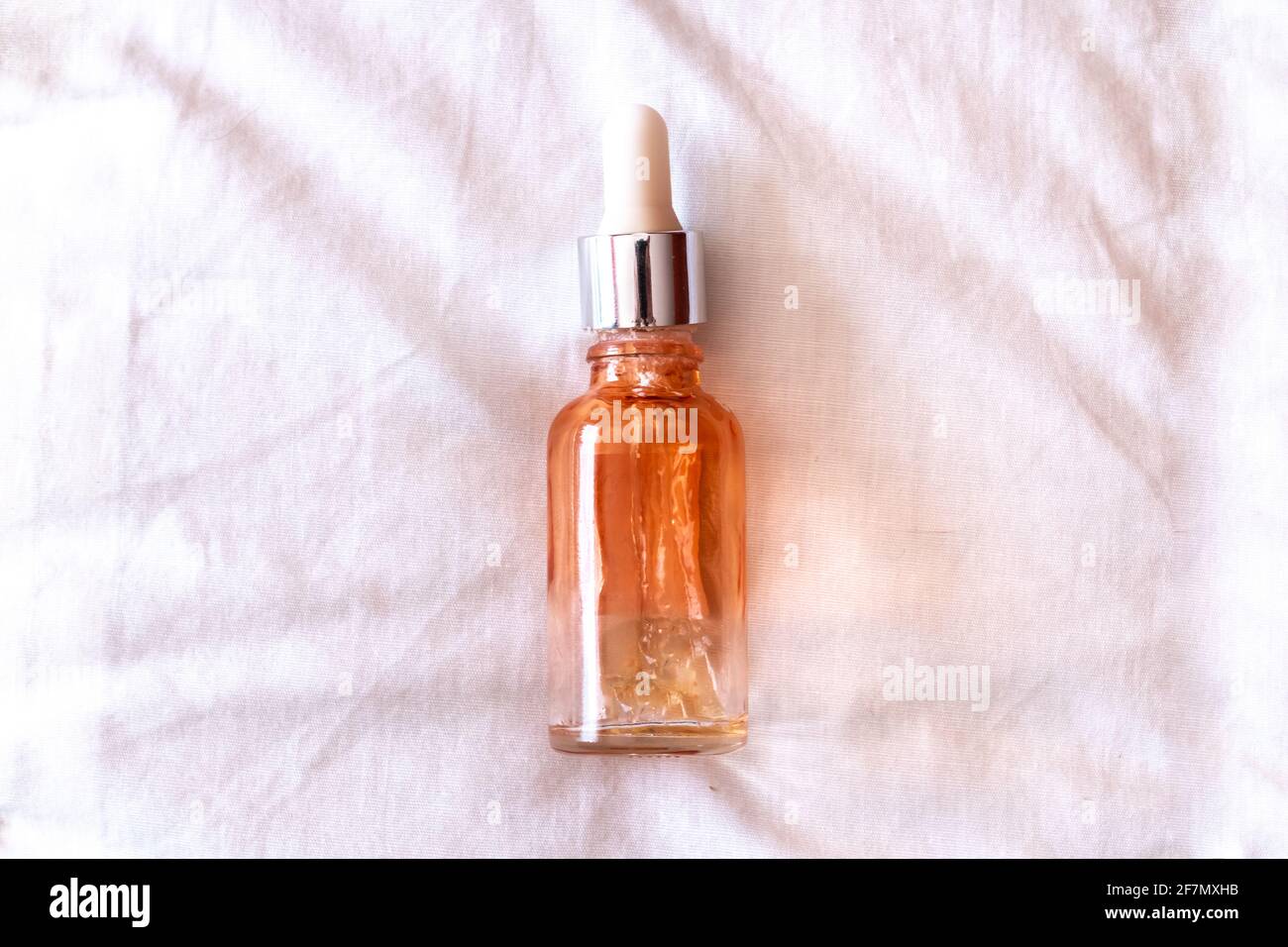 Eine leere Serumflasche mit orangefarbenem Farbton und weißem Tropferkopf, leicht abgeschraubt, auf einem weißen Stoff, isoliert, in Kanada während der Winterzeit. Stockfoto
