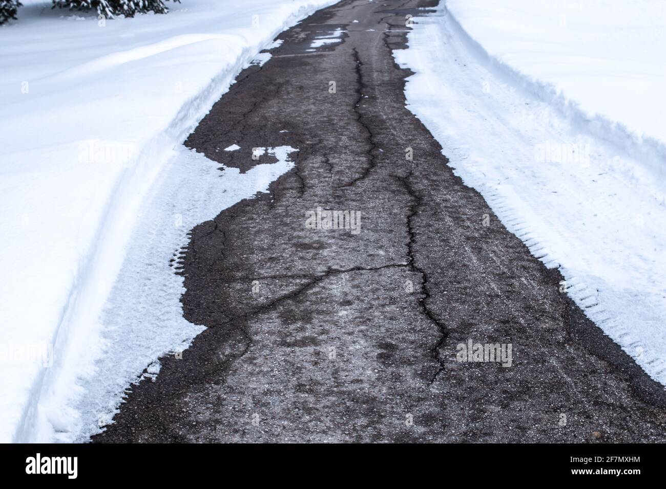 Gesprungener Asphalt auf einer Fahrt mitten im Winter, Schnee flankiert auf beiden Seiten der Straße in Ontario, Kanada, Februar 2021. Stockfoto