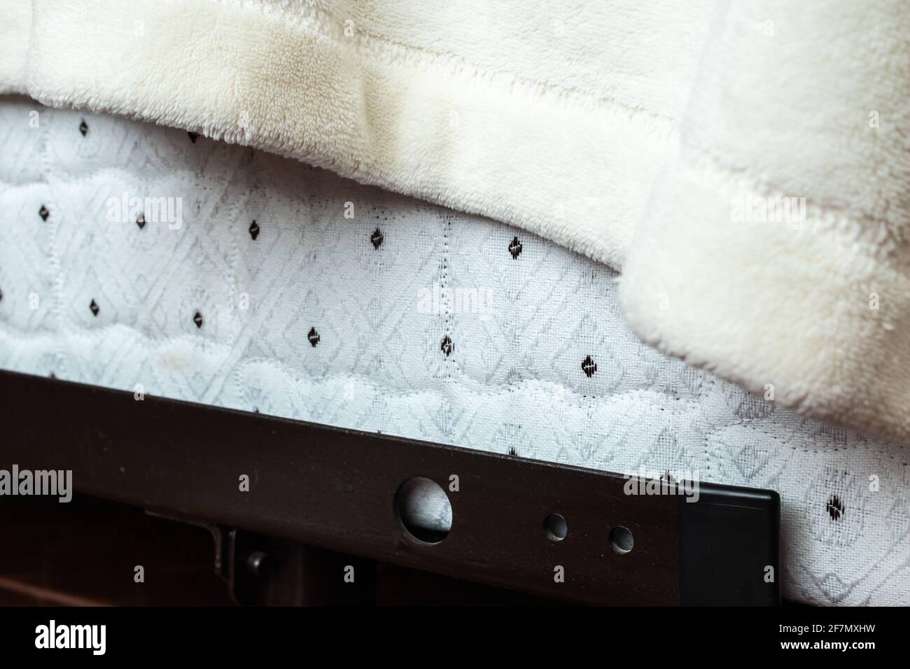 Aus nächster Nähe Ecke einer Bettdecke mit Bettmuster Feder mit schwarzen Punkten auf dem Stoff, bedeckt von einer drapierten fuzzy weißen Decke auf einem Stahlrahmen aus Metall. Stockfoto