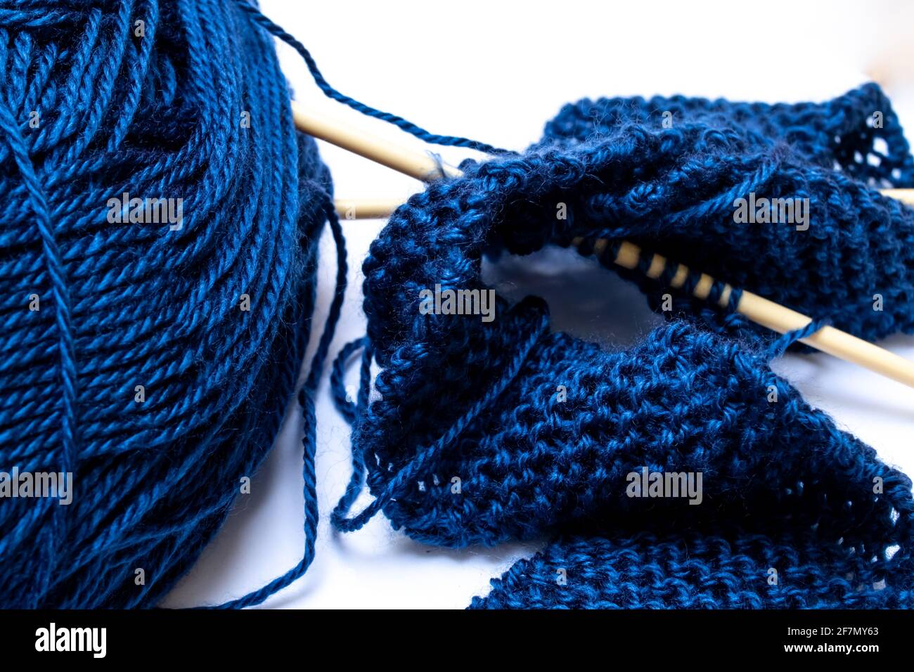 Mitternachtsblaues Garn, verworren und leicht verirrt neben beigefarbenen Stricknadeln, die einen kleinen klassischen Perlenstrick-Schal zusammenhalten. Stockfoto