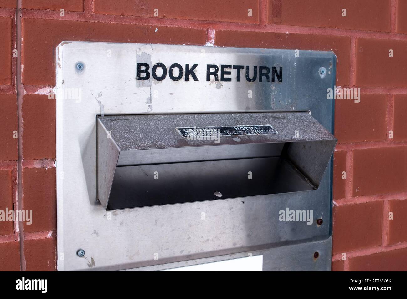 Ein alter, verwitterter, alter Metallbuch-Rückkehrcontainer in einer Backsteinmauer in der Londoner Innenstadt. Bücher lesen während der COVID-19-Pandemie. Stockfoto