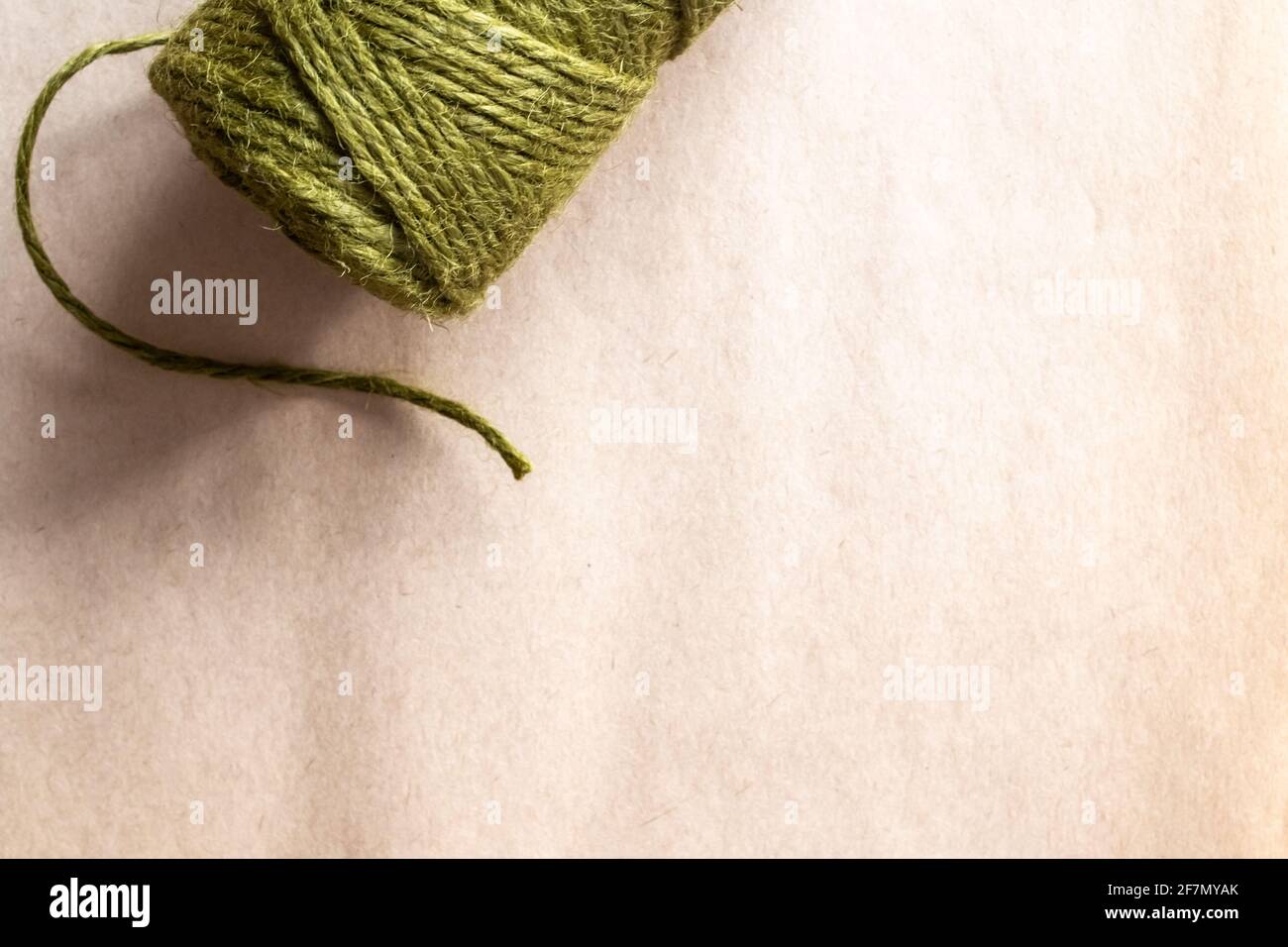 Ein Zylinder aus olivgrünem Garn mit einem einzelnen Strang, der bei natürlichem Licht auf einem Pergamentpapierhintergrund locker hängt, Ontario, Kanada, 2021. Speicherplatz kopieren. Stockfoto