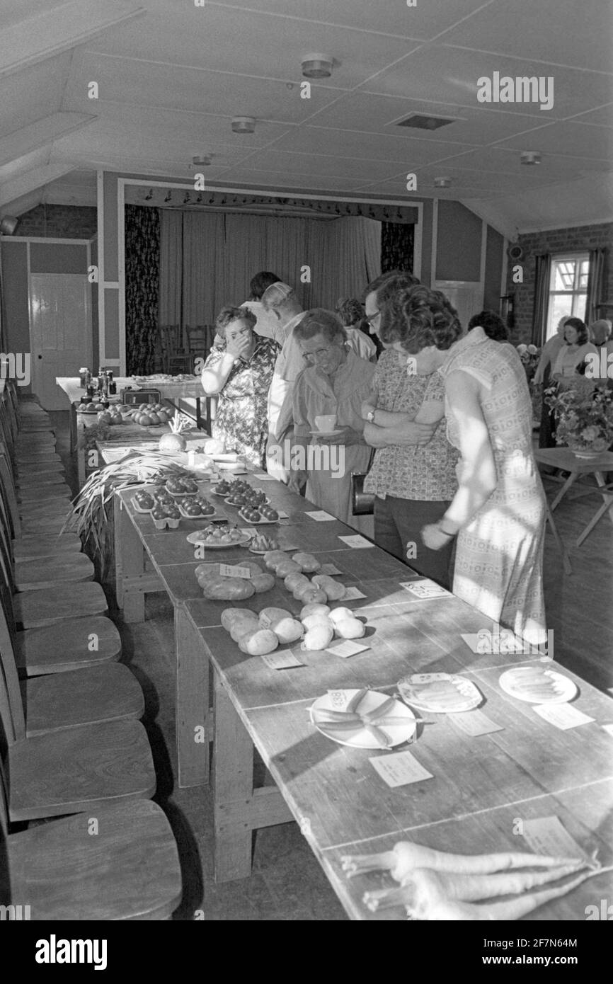 Leute, die Kuchen, Süßigkeiten, Marmeladen und Chutneys zum Verkauf suchen Bei indoor Kirchenhalle Fete bringen und kaufen Durcheinander Verkauf Ende der 1970er jahre in großbritannien Stockfoto