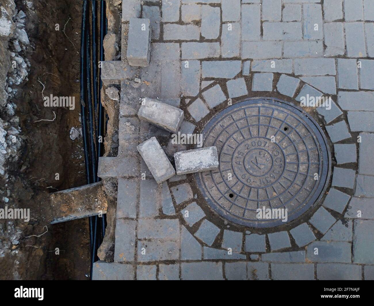 Kabelführung in einen Graben und Anschluss an eine Kanalisationsgrube, Abwasserkanäle mit Schlüpfkanal, Straßenbelag Stockfoto