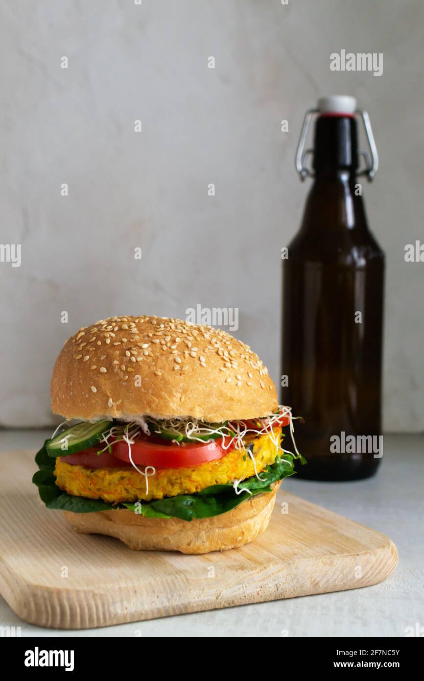 Vegetarischer Burger mit Kichererbsen, Mercovi, Zwiebeln und Knoblauchschnitzel mit einer Bierflasche auf dem Hintergrund. Vegetarisches Speisekonzept. Vertikale Ausrichtung. Stockfoto