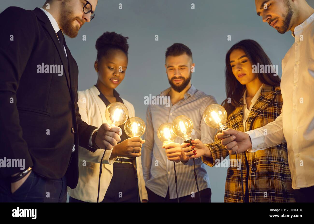 Interrassische Kollegen stellen helle Glühbirnen als Symbol für eine neue Geschäftsidee zusammen. Stockfoto