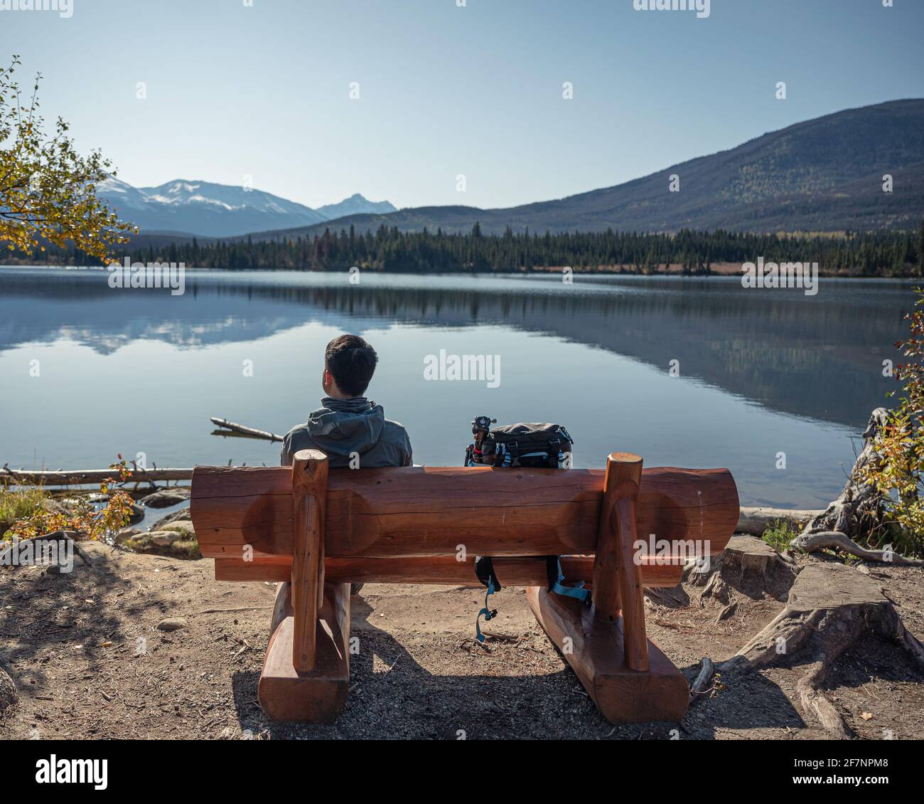 Junger Mann, der allein auf einer Holzbank am See am Pyramid Lake, Kanada, sitzt Stockfoto
