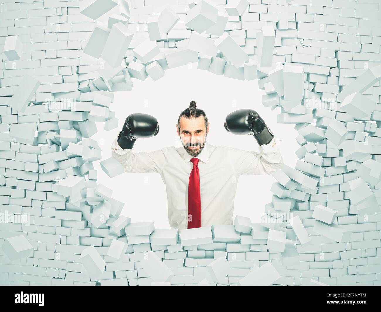 Geschäftsmann mit Boxhandschuhen bricht eine Mauer. Konzept der Stärke und Entschlossenheit. Stockfoto