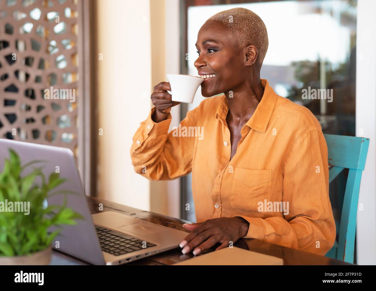 Afrikanische ältere Frau trinkt Kaffee, während sie in der Bar einen Laptop benutzt Restaurant: Intelligentes Arbeitskonzept Stockfoto