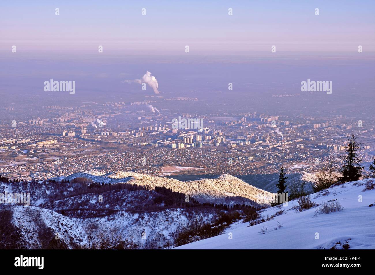 Stadt am Fuße der Berge bei Sonnenaufgang; Almaty Stadt, Kasachstan. Konzept der ökologischen Probleme Stockfoto