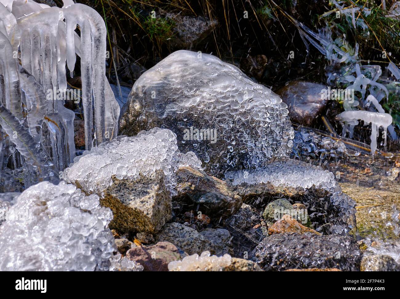 Große Eiskristalle auf Steinen in unmittelbarer Nähe zum Fluss; erste Herbstfröste und herannahende Winterkonzeption Stockfoto