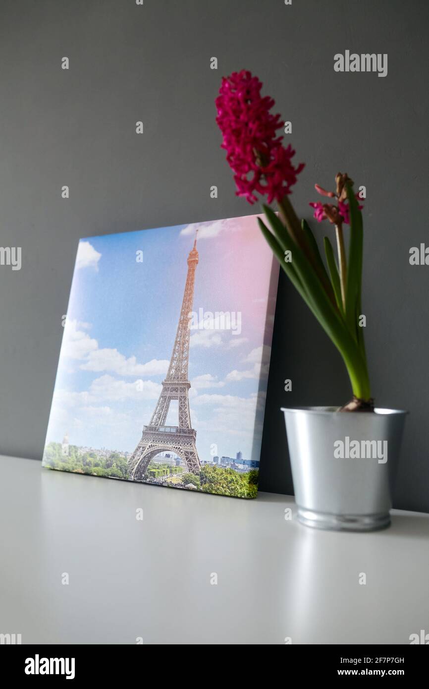 Leinwanddruck auf Rahmen mit Gallery Wrap auf grauem Wandhintergrund gestreckt. Fotografie mit dem Pariser Eiffelturm Stadtbild und Blume im Topf auf weißem Sch Stockfoto