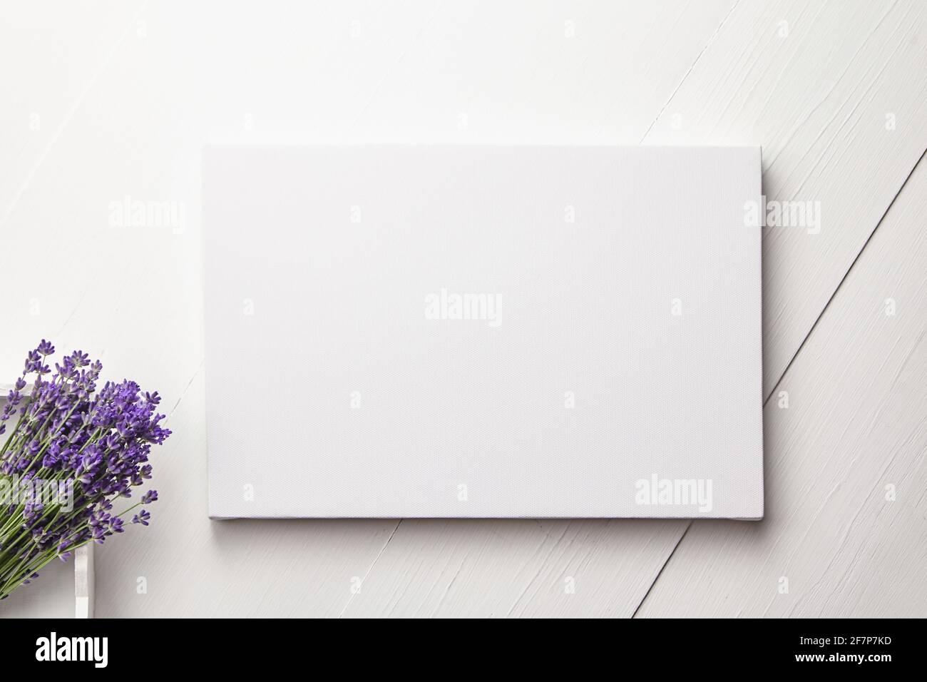 Weißes Canvas-Mockup und Lavendelblüten-Bouquet auf weißem Holztisch-Hintergrund, flach liegend. Leere Leinwand, Draufsicht Stockfoto