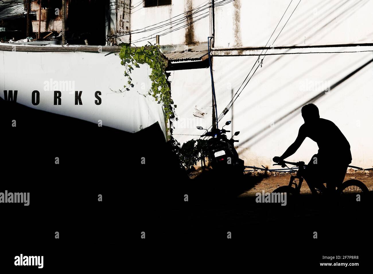 Ein junger Mann auf einem Mountainbike erscheint als Silhouette an einer sonnigen weißen Wand, auf der das Wort „Works“ steht: Boracay Island, Asien Stockfoto
