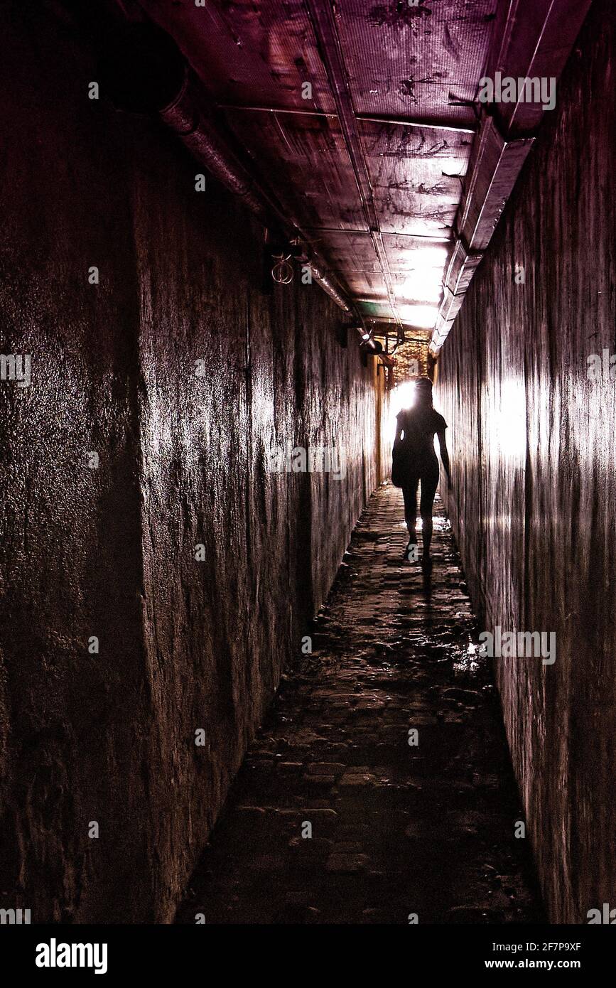 Silhouette einer jungen Frau in einem engen, dunklen Gehweg, die gegen das Licht am Ende des Tunnels geht, gesehen auf den Philippinen, Asien Stockfoto