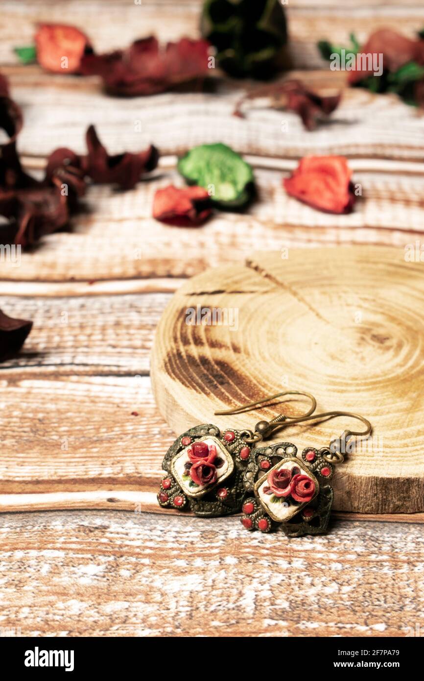 Vintage goldene Ohrringe mit dunkelroten Rosen auf Holztisch, mit Holzkissen und roten Blütenblättern Stockfoto