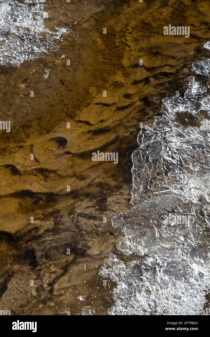 Frühlingsbach mit einem gemusterten Boden und Eiskruste auf Die Kanten der aktuellen Nahaufnahme Stockfoto