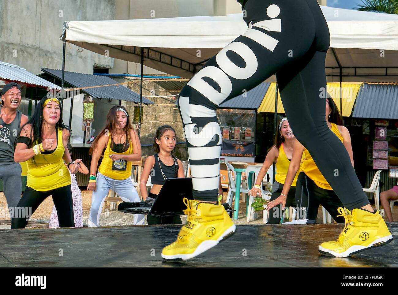 Eine Gruppe von Zumba-Tänzern, alle in gelber Sportkleidung gekleidet, trainiert fröhlich vor einer weiblichen Instruktorin auf einer Bühne auf der Insel Boracay, Asien Stockfoto