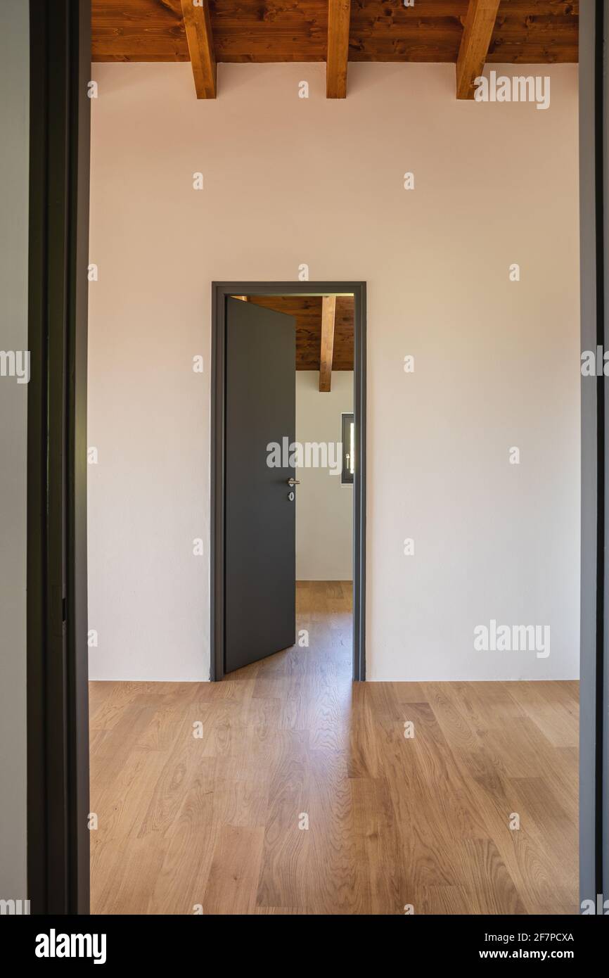 Detail eines offenen, leeren, weißen Zimmers mit freiliegenden Holzbalken und Hartholzböden. Niemand drinnen. Stockfoto