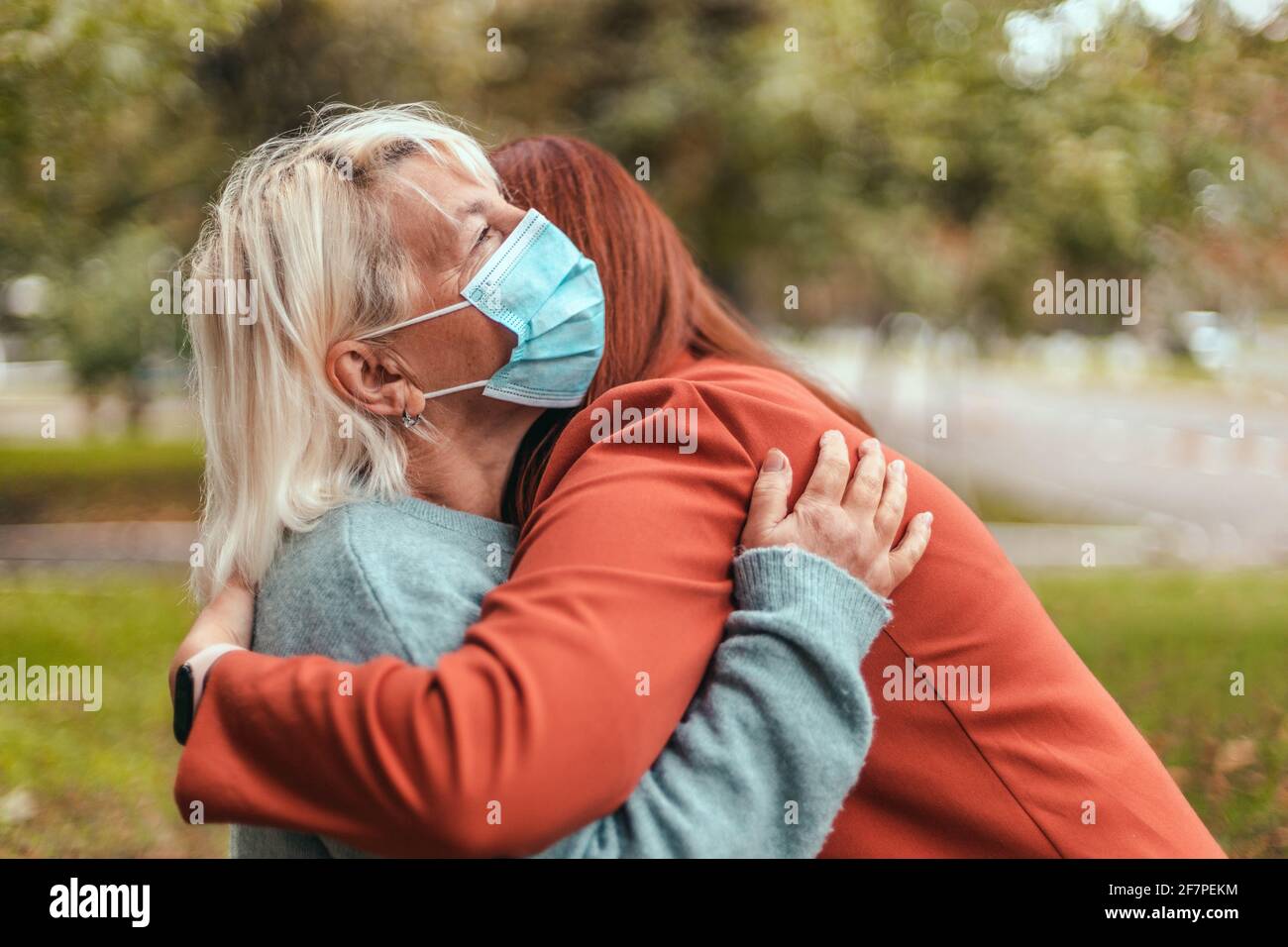 Familienumarmung Eine Erwachsene Frau senora in einem schützenden medizinischen Abstrich umarmt ihre Tochter im Park. Stockfoto