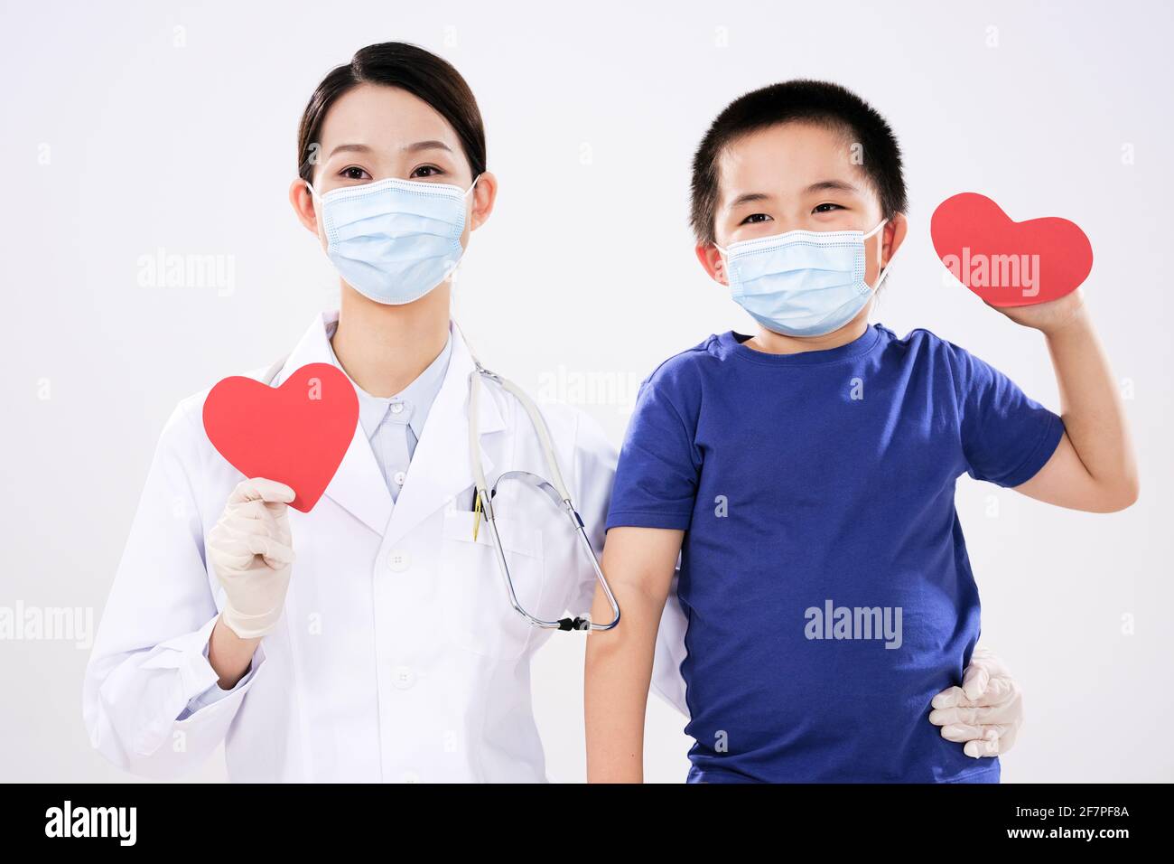 Eine Ärztin und ein kleiner Junge hatten jeweils einen Rotes Herz schaut auf die Kamera Stockfoto