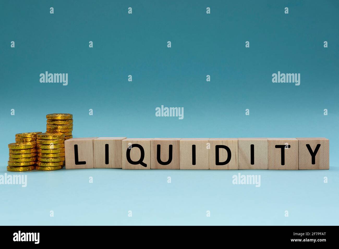 Liquiditätstext auf Holzblock mit einem Haufen Münzen Auf einem blau-weißen Hintergrund Stockfoto