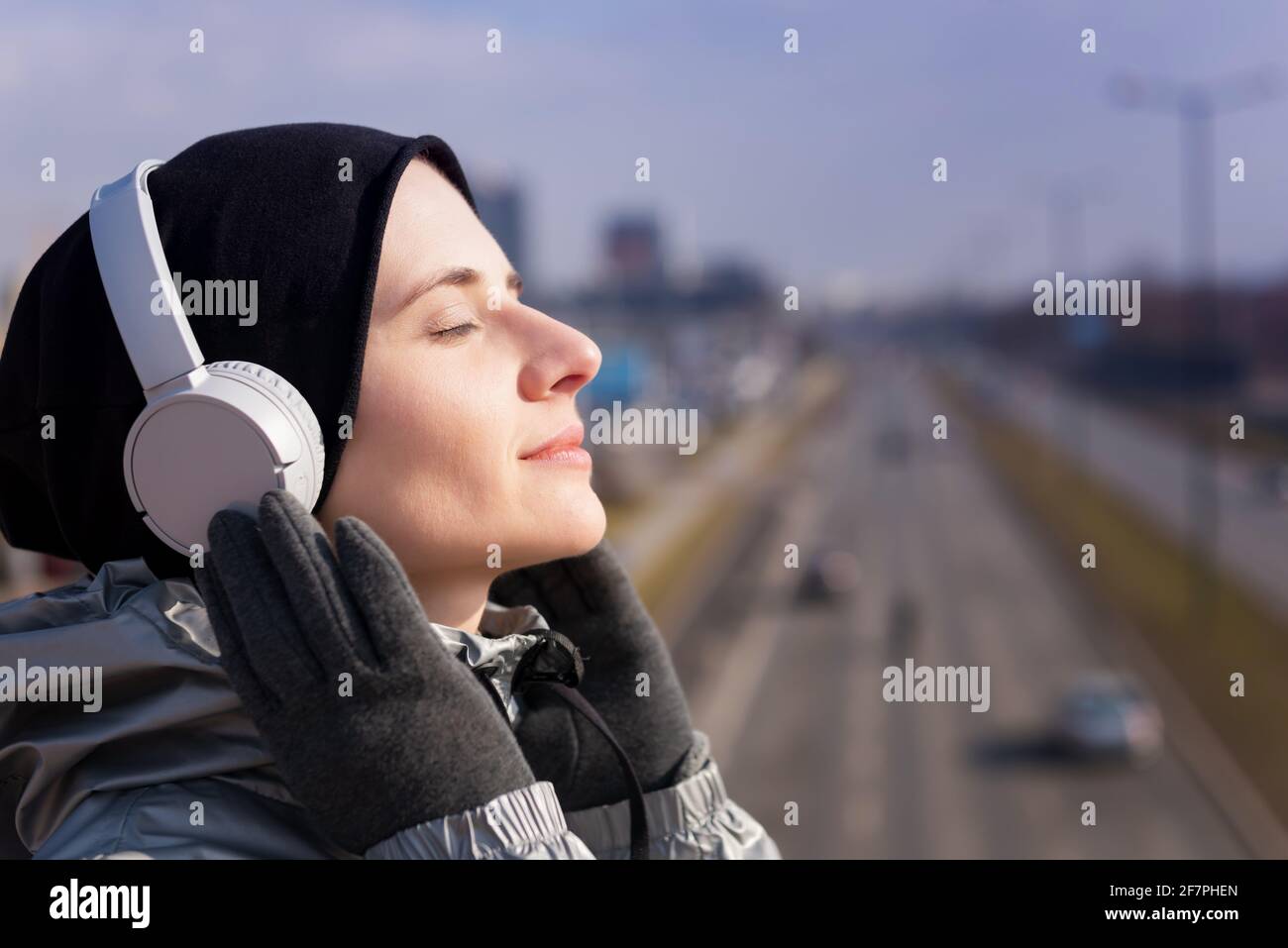 Lächelnd schöne junge Erwachsene Frau hören Musik mit ihr Smartphone und Kopfhörer zu Fuß durch die Stadt Stockfoto