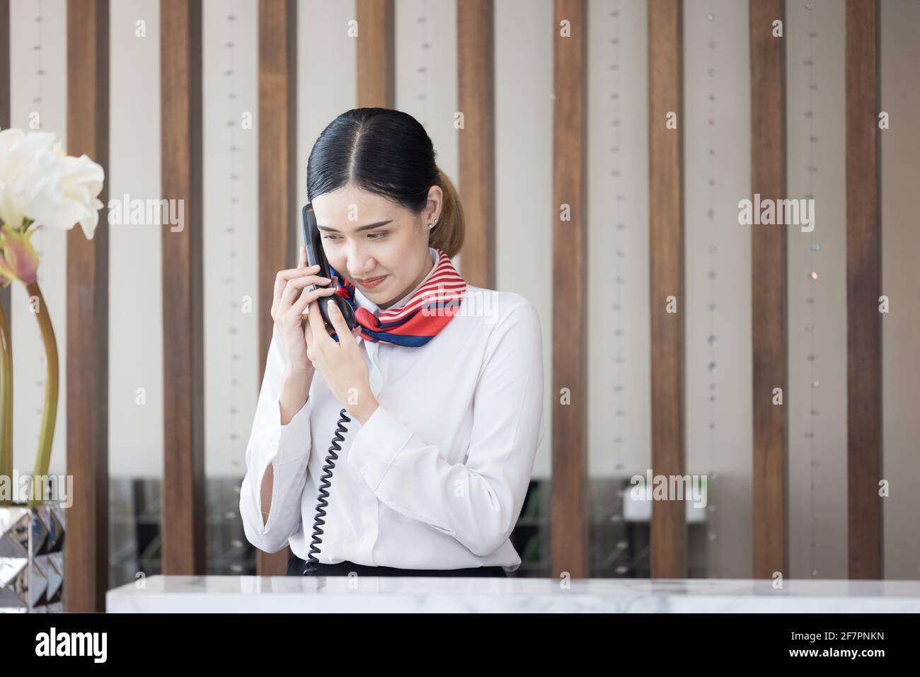 Willkommen im Hotel, glückliche junge asiatische Frau, Angestellte an der Rezeption Lächelnd stehend, nimmt sie einen Anruf an einer modernen Luxusrezeption an Zähler Stockfoto