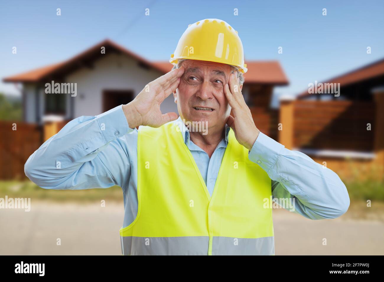 Älterer Bauherrn mit schockiert überrascht überfordert Ausdruck macht Geste Berührende Tempel im Hintergrund des Hausgebäudes Stockfoto