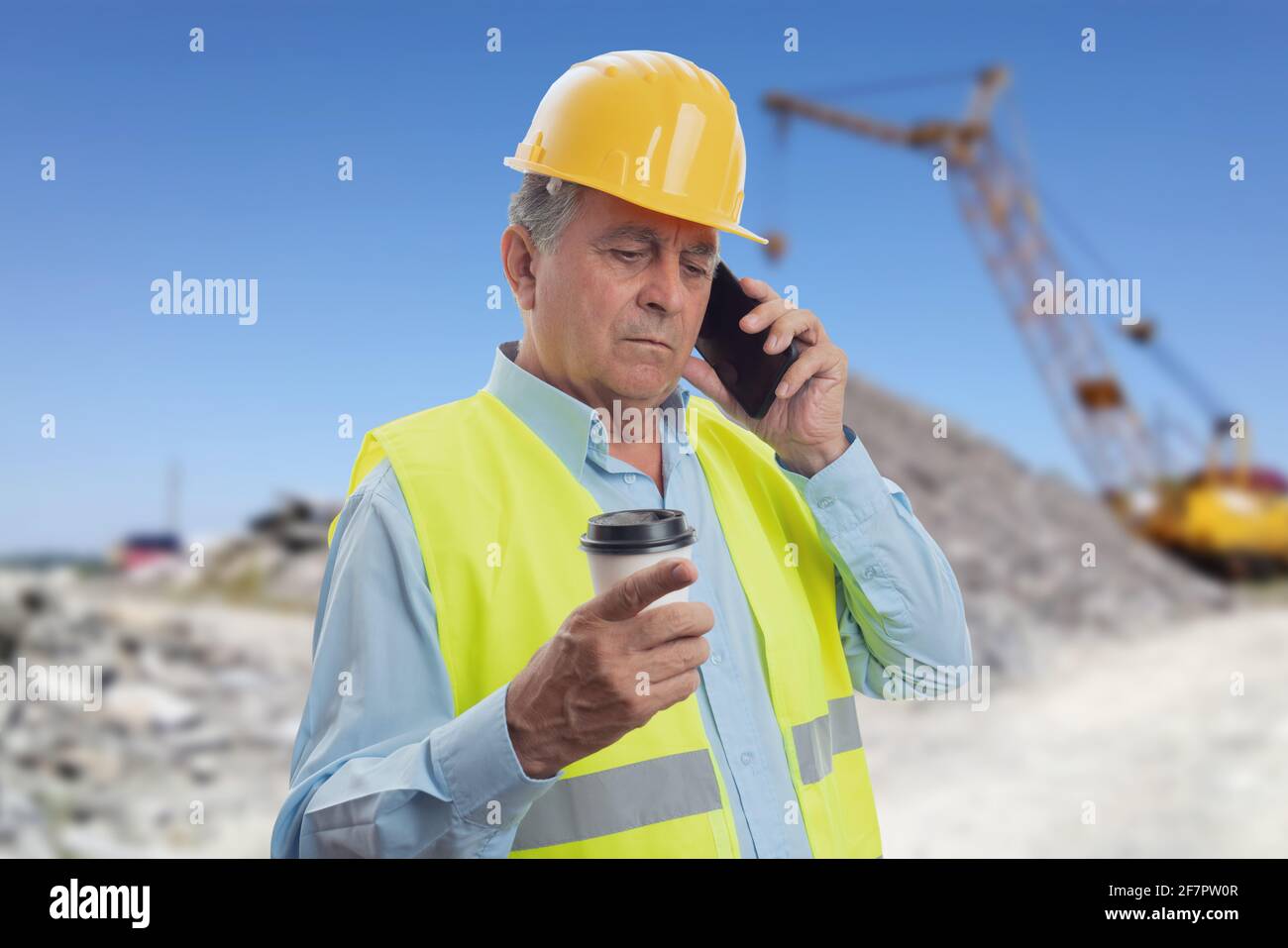 Alter Konstrukteur, der bei der Arbeit auf dem Smartphone spricht hardhat und Weste halten Kaffee in Take-away Papierbecher mit Baustelle Hintergrund Stockfoto