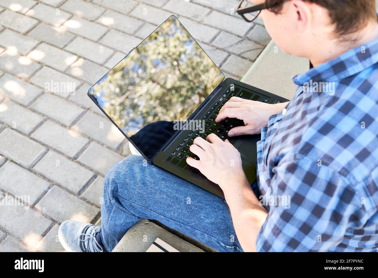 Junger Mann, der draußen auf einem Laptop tippt. Konzept des digitalen Nomaden, Arbeiten oder Studieren unter freiem Himmel. Stockfoto