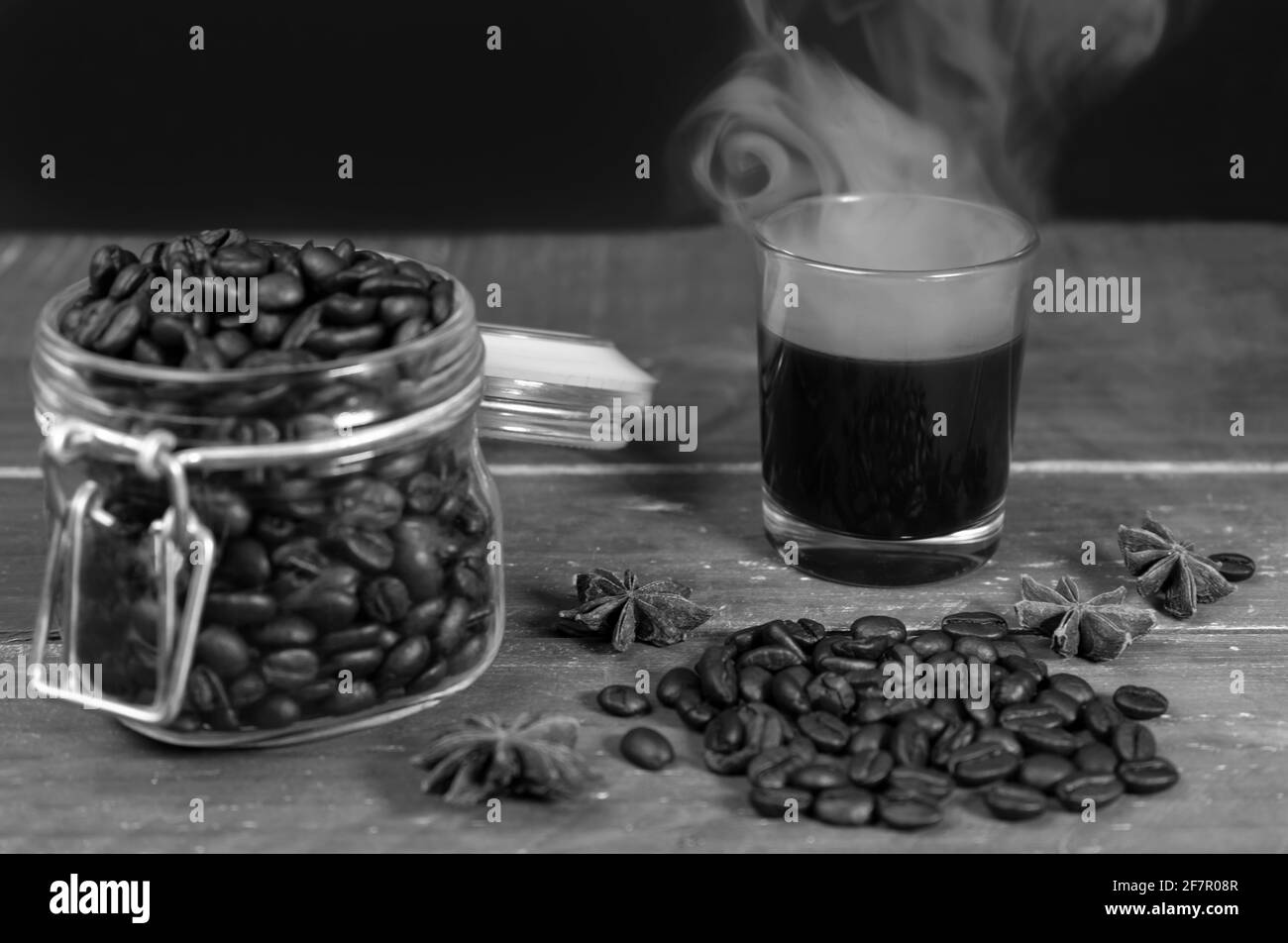 Heißer schwarzer Kaffee im Glas mit Rauch und Kaffeebohnen im Glas auf Holztisch.Nahaufnahme Schwarz-Weiß-Fotografie mit Kopierraum. Stockfoto