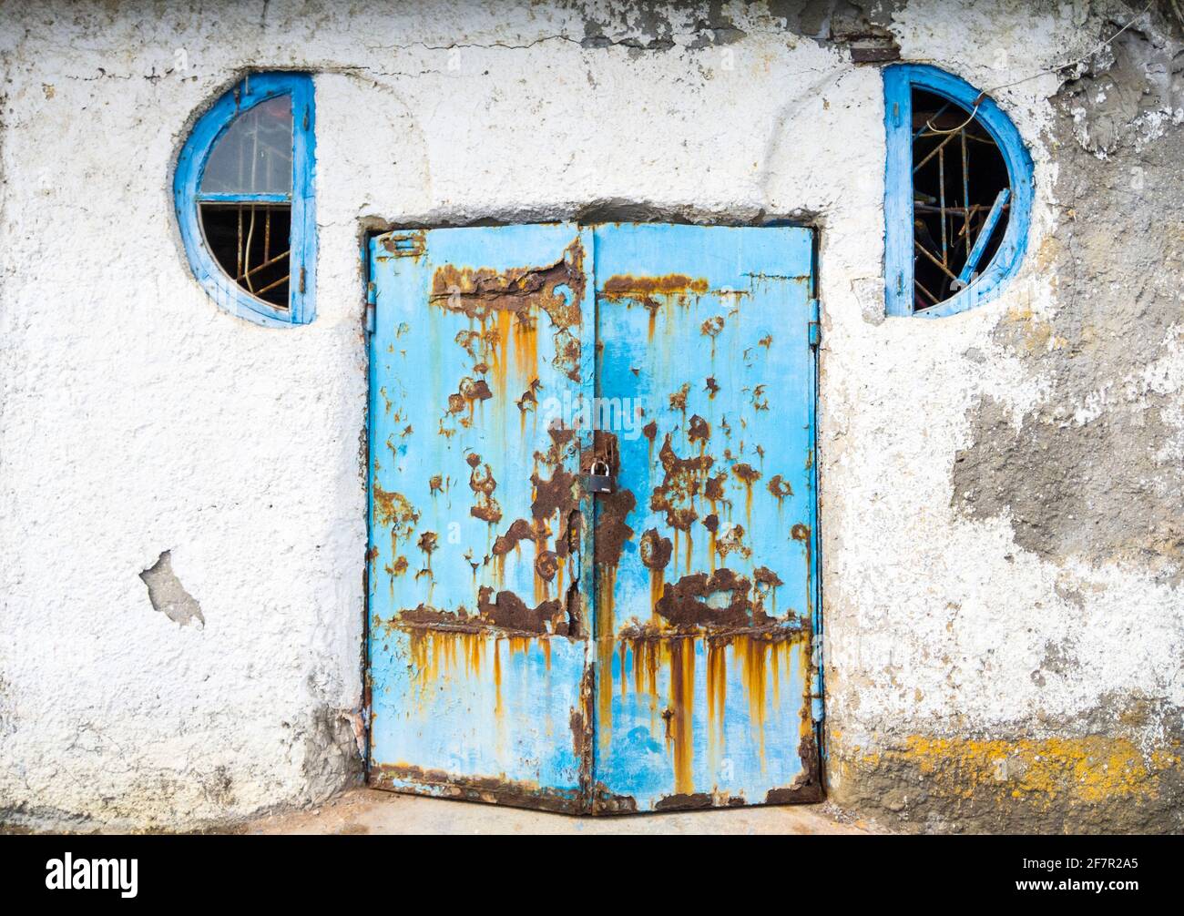Blick auf das Äußere eines stimmungsvollen Hauses. Alte, korrodierte, blaue Metalltür und eine weiße Wand. Stockfoto