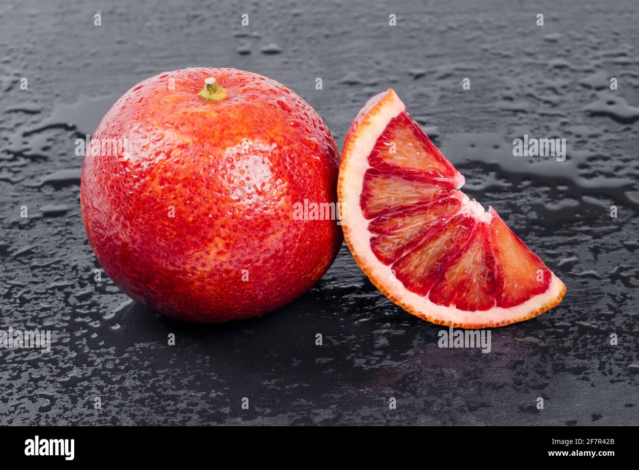 Blutige Orangen ganz und halbiert auf schwarzem Schieferbrett mit Wassertropfen. Rote sizilianische Orangenfrucht Stockfoto