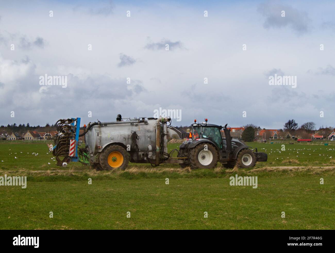 Traktor mit Gülletank und Gülleinjektor, im Hintergrund ein Dorf Stockfoto