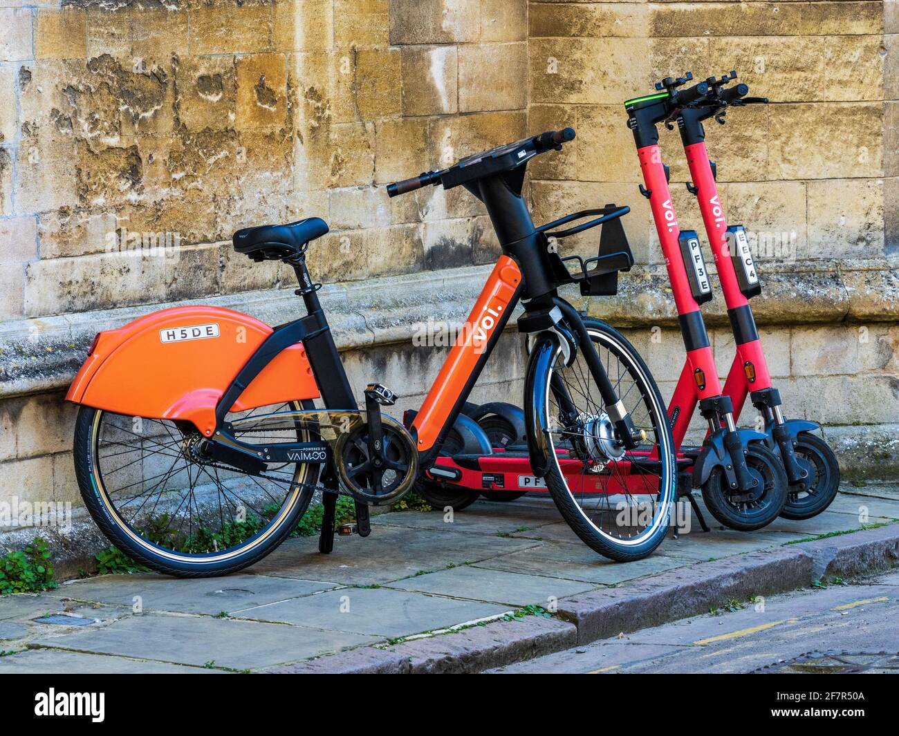 VOI Elektro-Scooter und E-Bikes können an einer Straße im historischen Zentrum von Cambridge gemietet werden. VOI Technology E-Scooter & E-Bikes auf einer Straße in Cambridge Stockfoto