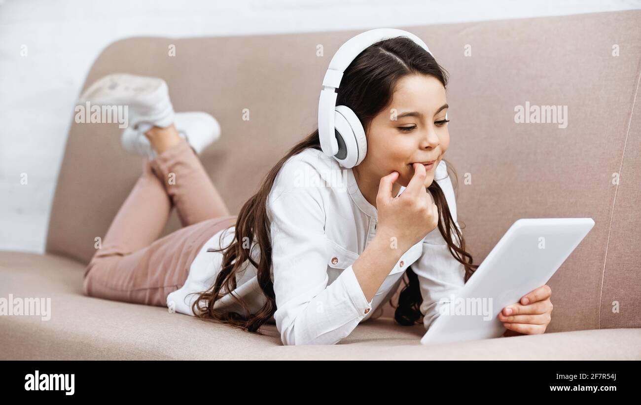 Lächelndes Kind mit Kopfhörern und digitalem Tablet auf der Couch Wohnzimmer Stockfoto
